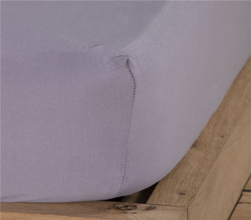 Κοντινή λήψη από τη γωνία στρώματος με εφαρμοσμένο ανοιχτό γκρι jersey σεντόνι με λάστιχο, δείχνοντας την εφαρμογή του υφάσματος.υφάσματος.