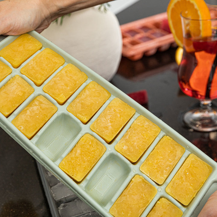 Παγοθήκες με παγάκια και φρούτα σε μαύρο πάγκο κουζίνας, με φόντο λευκό τοίχο και διακόσμηση.