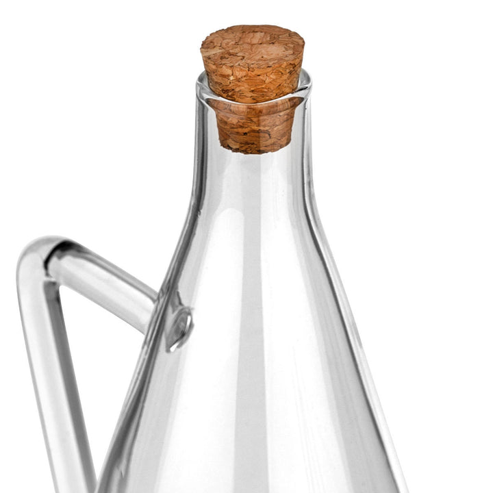 Κοντινή λήψη σε διαφανής γυάλινη κανάτα λαδιού με μακρύ στόμιο και χερούλι, σε λευκό φόντο, με minimal και κομψό σχεδιασμό.