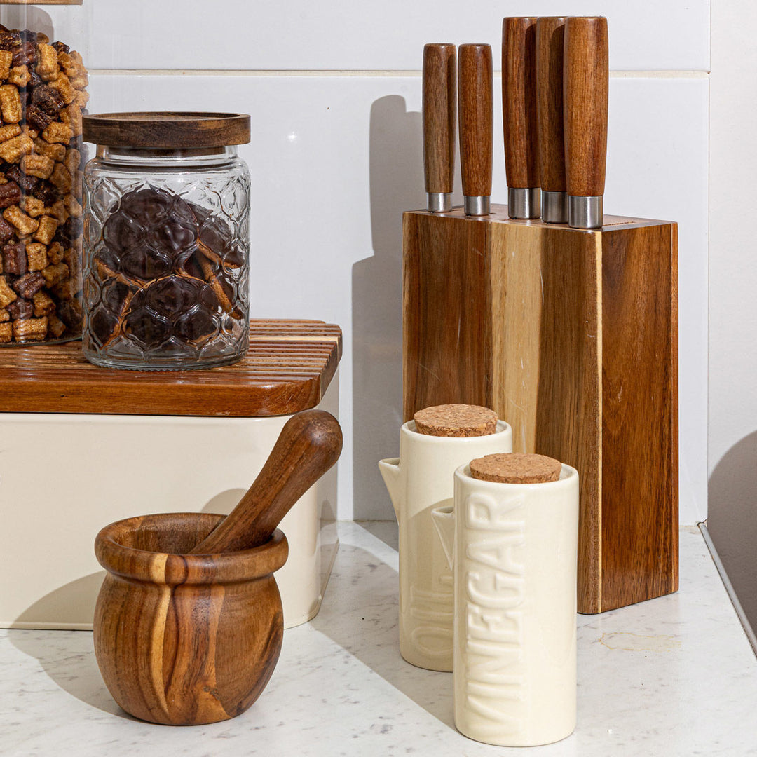 Κεραμικά δοχεία λαδιού και ξιδιού σε ιβουάρ απόχρωση με φελλό, τοποθετημένα σε οργανωμένο πάγκο κουζίνας με ξύλινα αξεσουάρ.