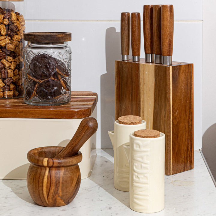 Κεραμικά δοχεία λαδιού και ξιδιού σε ιβουάρ απόχρωση με φελλό, τοποθετημένα σε οργανωμένο πάγκο κουζίνας με ξύλινα αξεσουάρ.