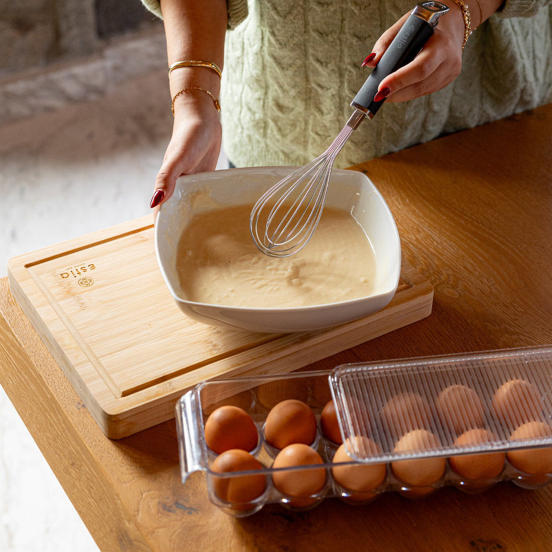 Το κουτί αυγών Estia τοποθετημένο σε ξύλινο πάγκο με καπάκι, μπροστά από σκηνή προετοιμασίας συνταγής.