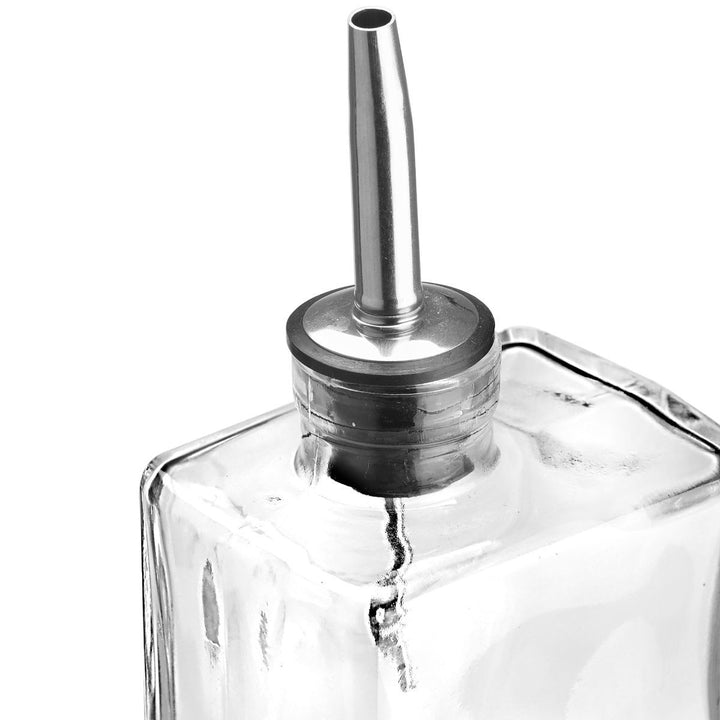 Κοντινή λήψη από γυάλινο δοχείο λαδιού με μεταλλικό στόμιο και καπάκι, σε λιτό σχεδιασμό, φωτογραφημένο σε λευκό φόντο για χρήση σε κουζίνα.