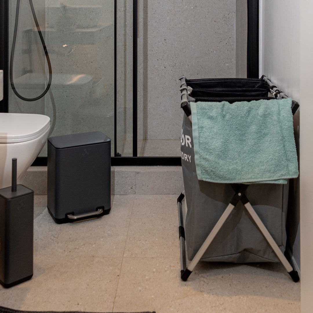 Καλάθι άπλυτων Estia τοποθετημένο σε μοντέρνο μπάνιο δίπλα σε ντουζιέρα και κάδο.