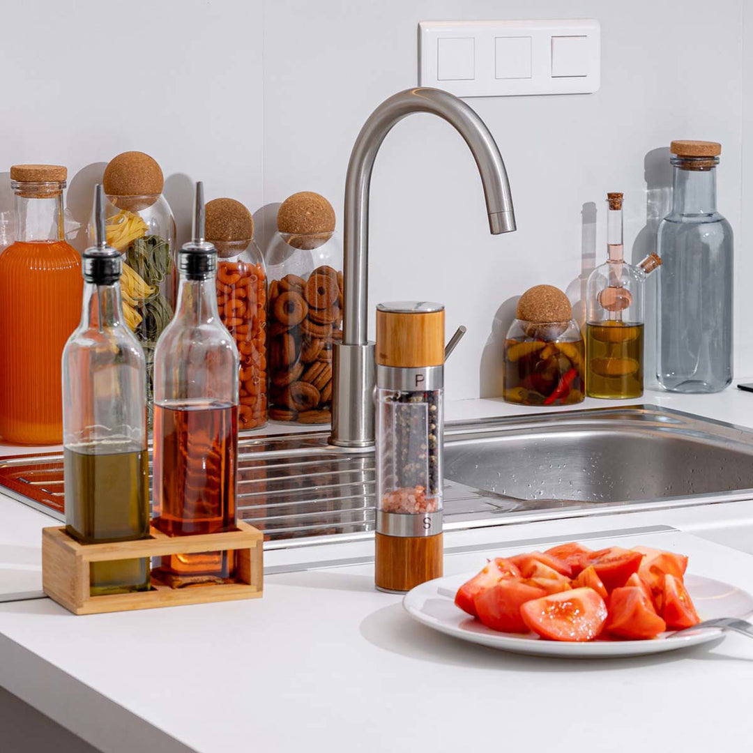 Σύνθεση κουζίνας με γυάλινα δοχεία λαδιού και ξυδιού, μύλο αλατιού και κομμένες ντομάτες σε λευκό πιάτο.