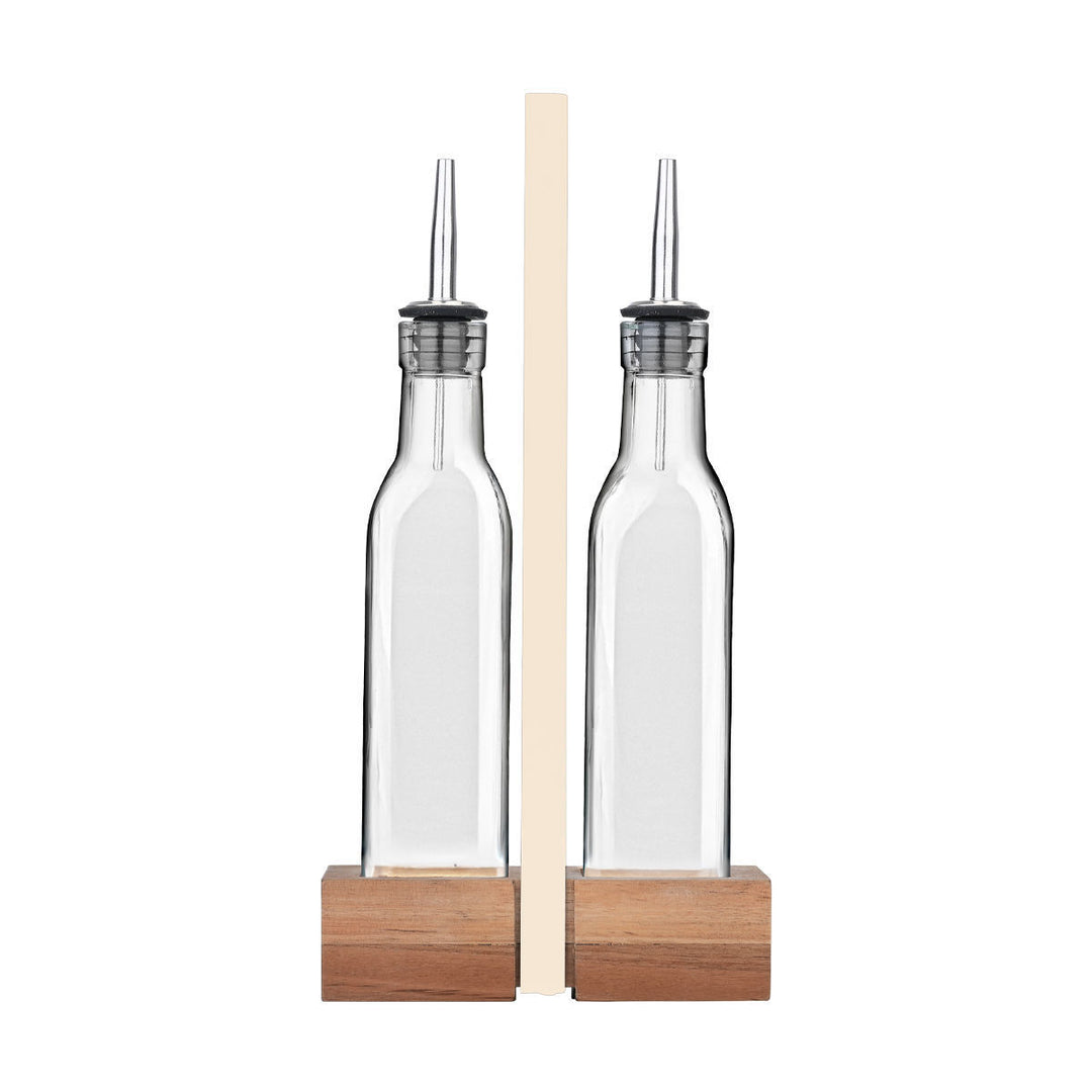 Μπροστά όψη από σετ δύο γυάλινων μπουκαλιών λαδιού με μεταλλικό ρύγχος pourer, τοποθετημένα σε ξύλινη βάση, σε λευκό φόντο, με κομψό και μίνιμαλ σχεδιασμό για την κουζίνα ή το τραπέζι.