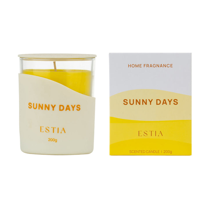 Αρωματικό κερί Sunny Days της Estia σε γυάλινο δοχείο με κίτρινο κερί και λευκό διακοσμητικό περίβλημα.