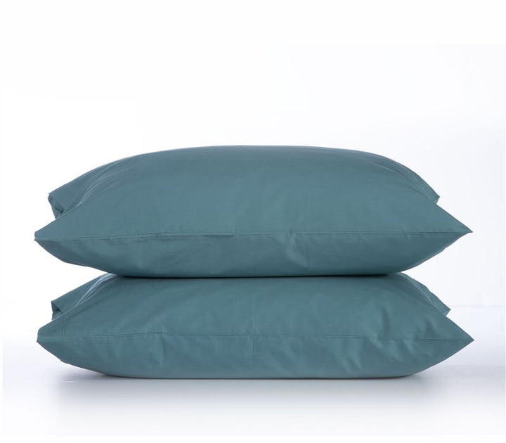 Δύο μαξιλαροθήκες σε απόχρωση dusty petrol, τοποθετημένες η μία πάνω στην άλλη, με ουδέτερο λευκό φόντο που αναδεικνύει το χρώμα και την υφή του υφάσματος