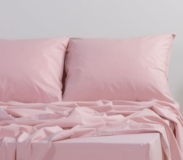 Ροζ μαξιλαροθήκες και σεντόνι σε minimal υπνοδωμάτιο, με απλωμένο ύφασμα που δημιουργεί απαλή, ανάλαφρη αίσθηση στον χώρο.