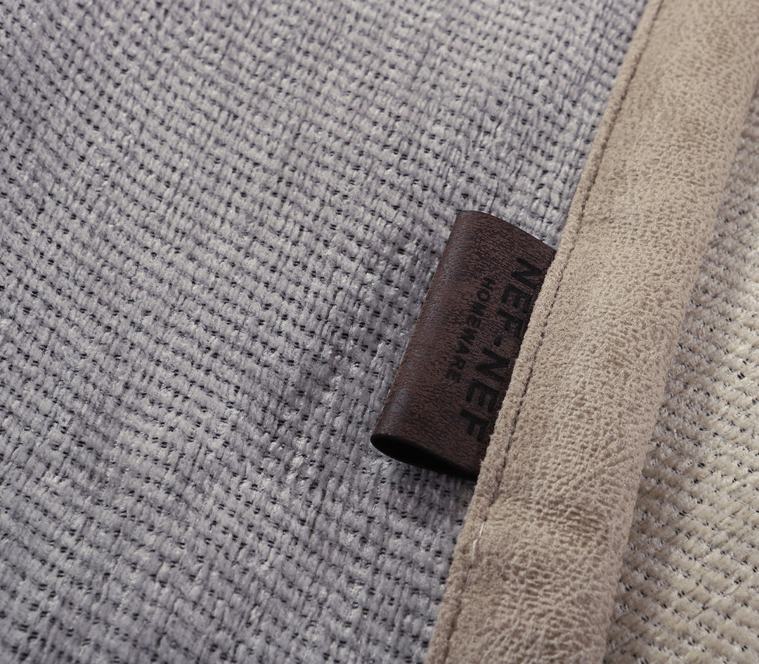 Κοντινή λεπτομέρεια από γκρι ριχτάρι καναπέ με υφή υφάσματος και δερμάτινη ετικέτα της εταιρείας Nef Nef Homeware.