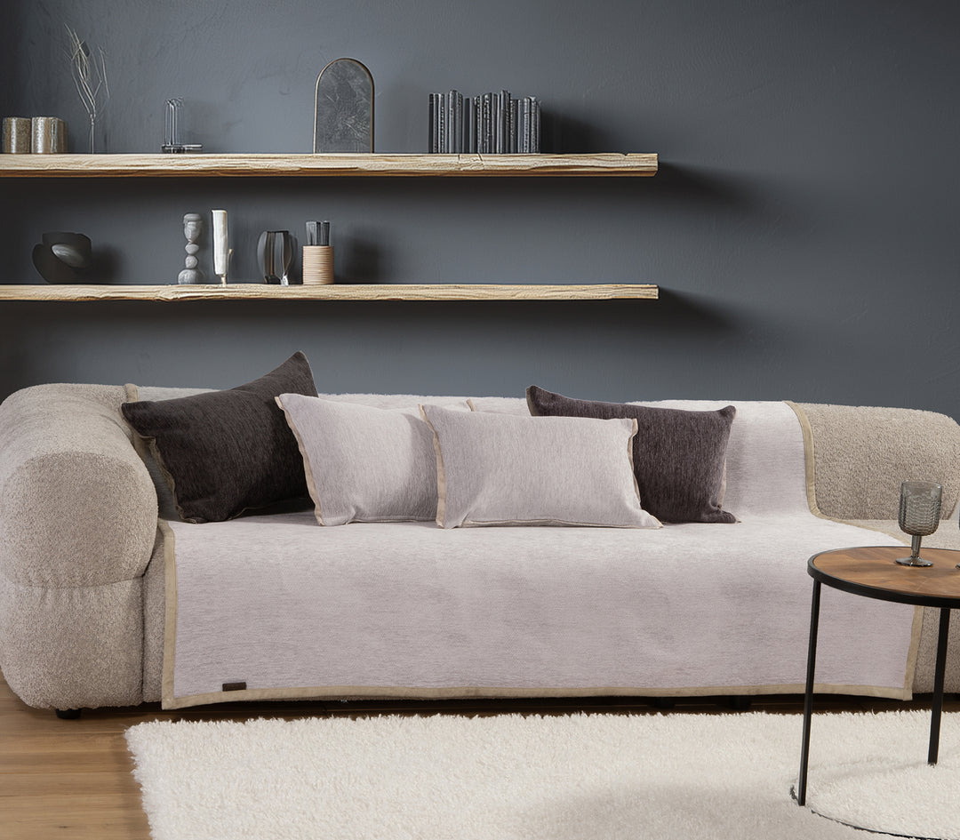 Μοντέρνος καναπές με ανοιχτό γκρι ριχτάρι και μαξιλάρια σε γκρι και σκούρο καφέ χρώμα, σε σαλόνι με γκρι τοίχο και διακοσμητικά ράφια.