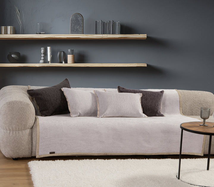 Μοντέρνος καναπές με ανοιχτό γκρι ριχτάρι και μαξιλάρια σε γκρι και σκούρο καφέ χρώμα, σε σαλόνι με γκρι τοίχο και διακοσμητικά ράφια.