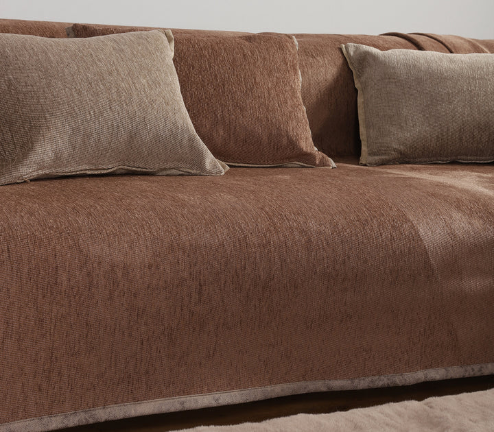 Καφέ ριχτάρι καναπέ με μαξιλάρια σε καφέ και μπεζ αποχρώσεις, τοποθετημένα σε καναπέ με ουδέτερο χαλί.