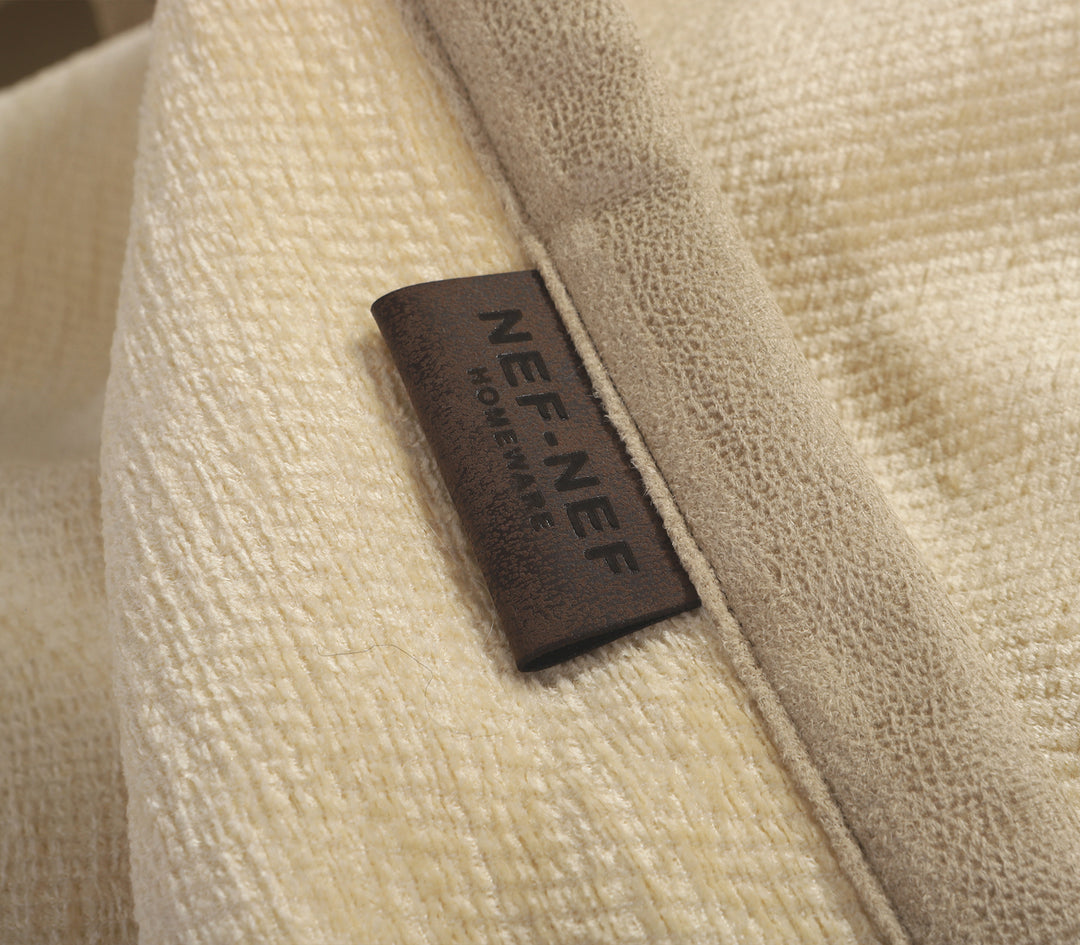 Εκρού ριχτάρι καναπέ με συνδυασμό μαξιλαριών σε καφέ και εκρού αποχρώσεις.