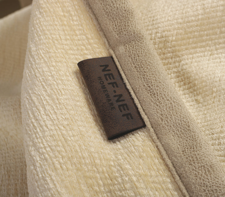 Κοντινή λεπτομέρεια σε εκρού ριχτάρι καναπέ με ταμπελάκι της εταιρείας Nef Nef Homeware σε δερμάτινη υφή.