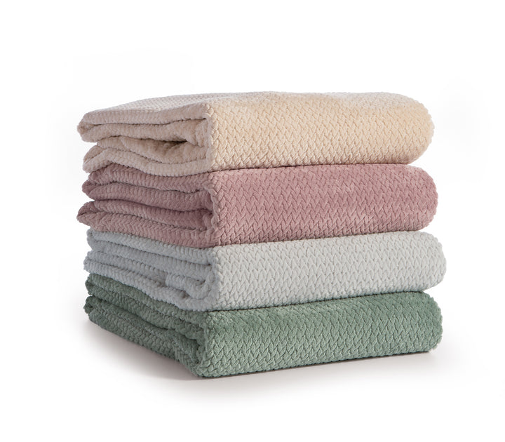 Στοίβα από κουβέρτες fleece σε εκρού, ροζ, γκρι και πράσινη απόχρωση με υφή ζιγκ-ζαγκ.
