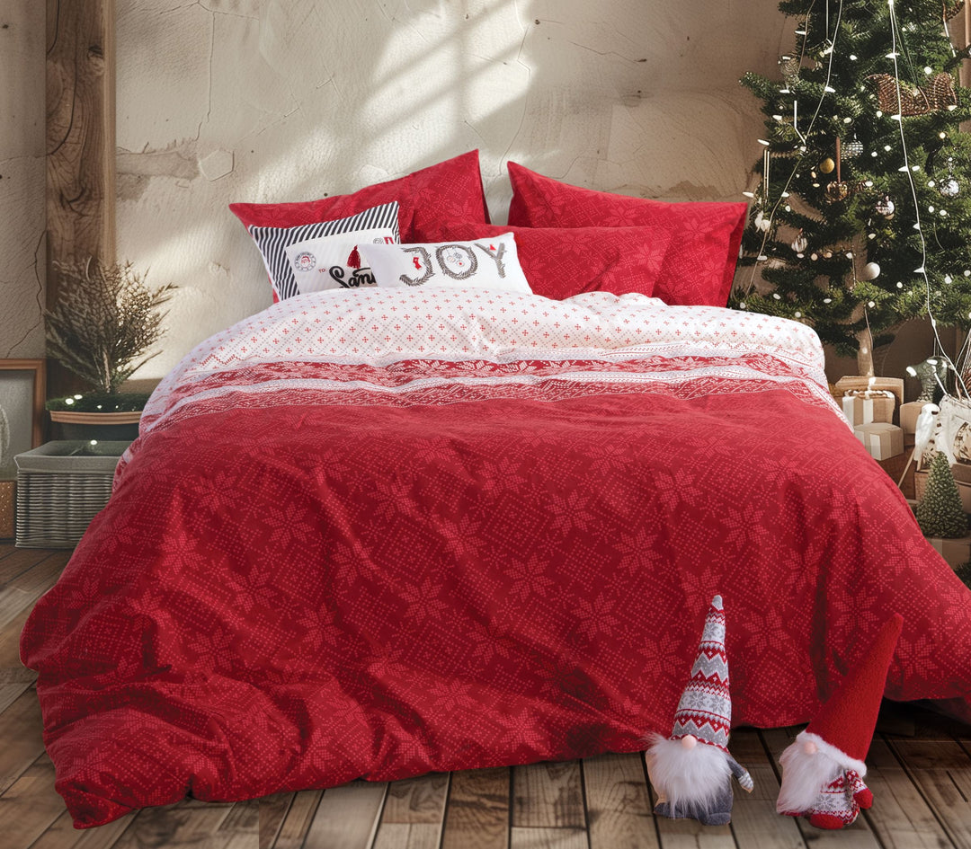 Κρεβάτι στολισμένο με χριστουγεννιάτικο σετ σεντόνια σε κόκκινο και λευκό χρώμα, με νιφάδες και παραδοσιακά σχέδια, δίπλα σε χριστουγεννιάτικο δέντρο.