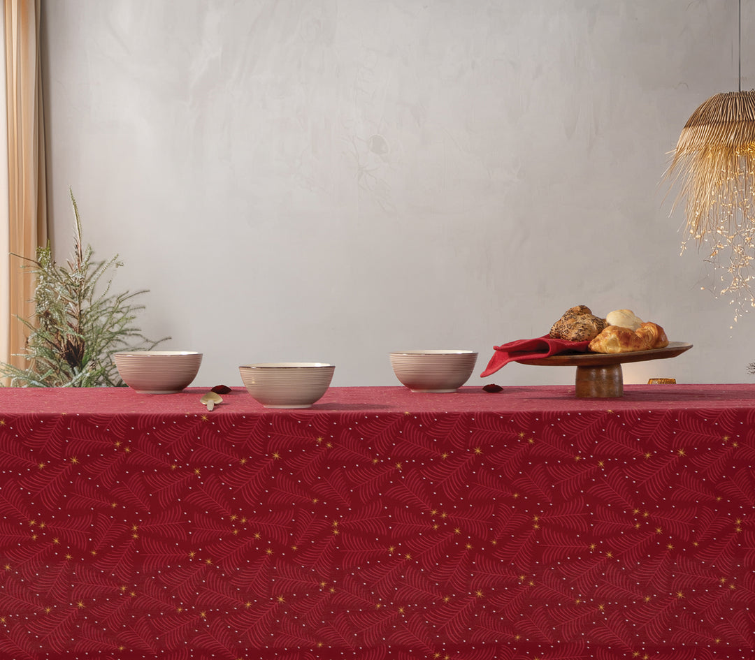 Χριστουγεννιάτικο τραπέζι διακοσμημένο με κόκκινο τραπεζομάντηλο με μοτίβο χρυσών αστεριών και κλαδιών, επάνω του κεραμικά μπολ και πιατέλα με ψωμάκια σε γιορτινή ατμόσφαιρα.
