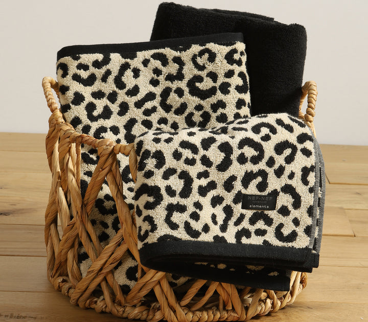Σετ πετσετών μπάνιου με leopard animal print σε μπεζ και μαύρο χρώμα, τοποθετημένες σε ψάθινο καλάθι πάνω σε ξύλινη επιφάνεια.