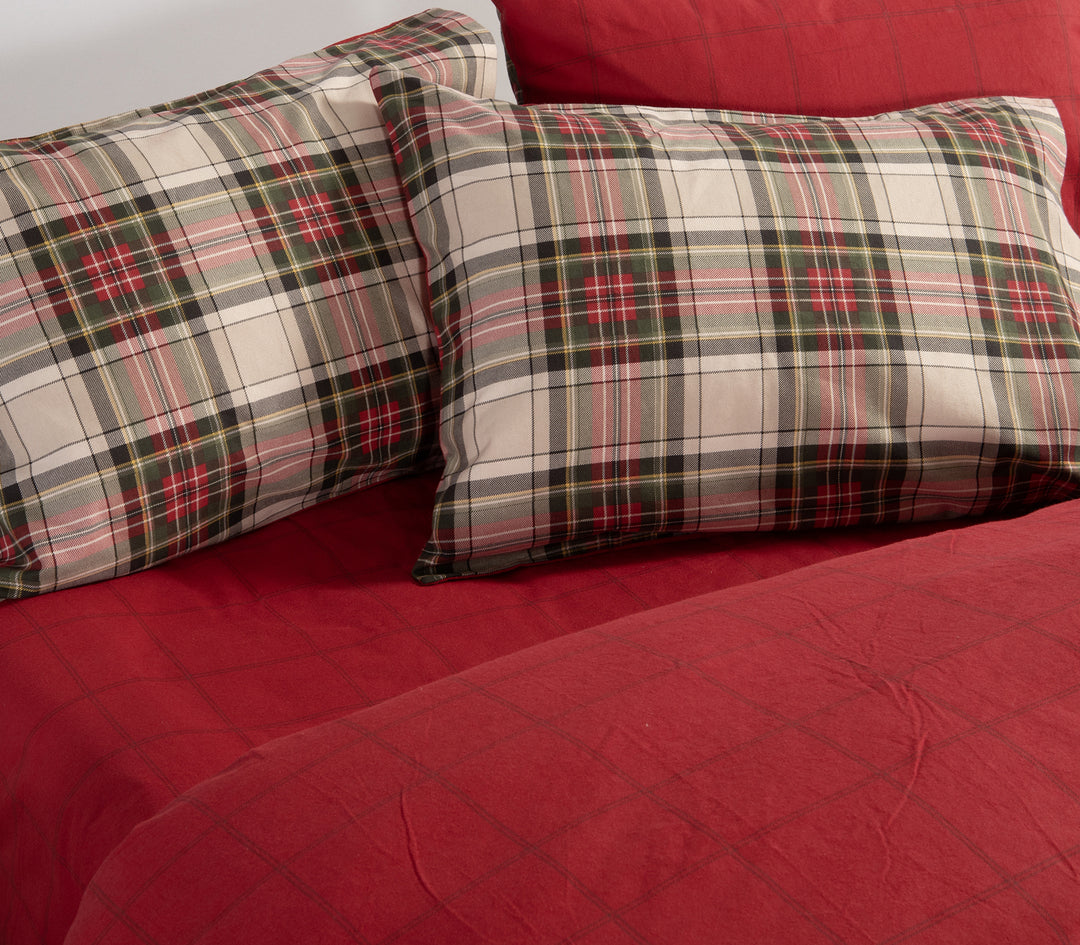 Κρεβάτι στρωμένο με σετ σεντόνια καρό σε κόκκινες και πράσινες αποχρώσεις, με μαξιλαροθήκες στο ίδιο μοτίβο και κόκκινο κατωσέντονο, της εταιρείας Nef Nef Homeware.