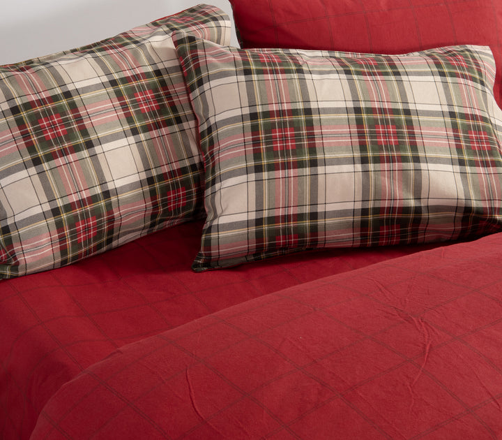 Κρεβάτι στρωμένο με σετ σεντόνια καρό σε κόκκινες και πράσινες αποχρώσεις, με μαξιλαροθήκες στο ίδιο μοτίβο και κόκκινο κατωσέντονο, της εταιρείας Nef Nef Homeware.