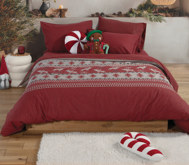 Υπνοδωμάτιο διακοσμημένο με σετ σεντόνια και παπλωματοθήκη σε κόκκινες και μπεζ αποχρώσεις με σχέδιο ελαφάκια και δέντρα, δημιουργώντας ζεστή χριστουγεννιάτικη ατμόσφαιρα, της εταιρείας Nef Nef Homeware.