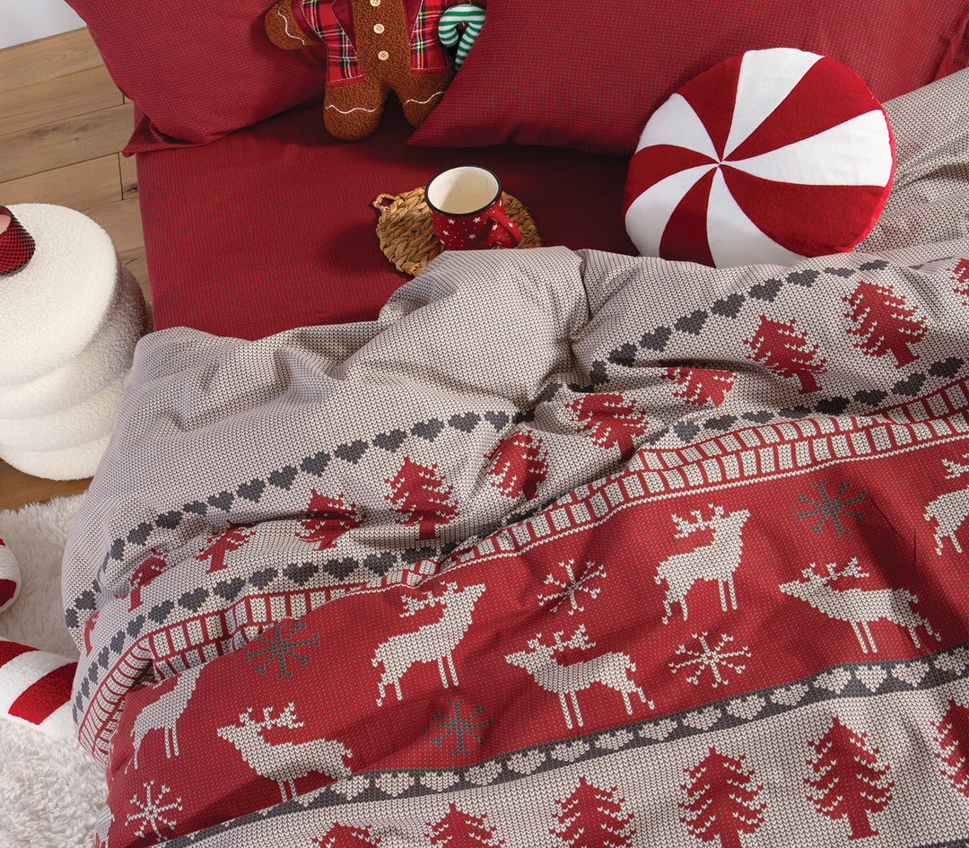 Κρεβάτι με κόκκινα σεντόνια και παπλωματοθήκη σε μοτίβο πλεκτού με ελαφάκια και δέντρα σε μπεζ και κόκκινες αποχρώσεις, της εταιρείας Nef Nef Homeware.