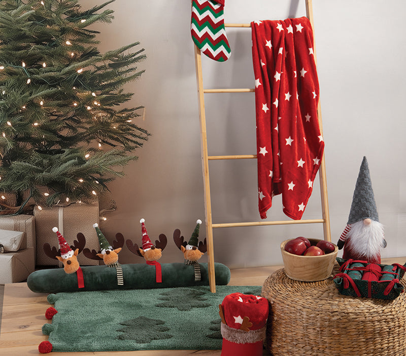 Χριστουγεννιάτικη διακόσμηση σαλονιού με πράσινο δέντρο, κόκκινη κουβέρτα με λευκά αστέρια, και διακοσμητικά με θέμα τάρανδο και νάνο σε γιορτινά χρώματα κόκκινο και πράσινο.