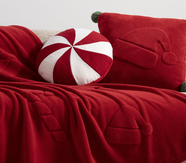 Χριστουγεννιάτικη διακόσμηση καναπέ με κόκκινη κουβέρτα και μαξιλάρι με σχέδιο σκούφου Άγιου Βασίλη, συνοδευόμενα από στρογγυλό μαξιλάρι τύπου ζαχαρωτού σε κόκκινο και λευκό