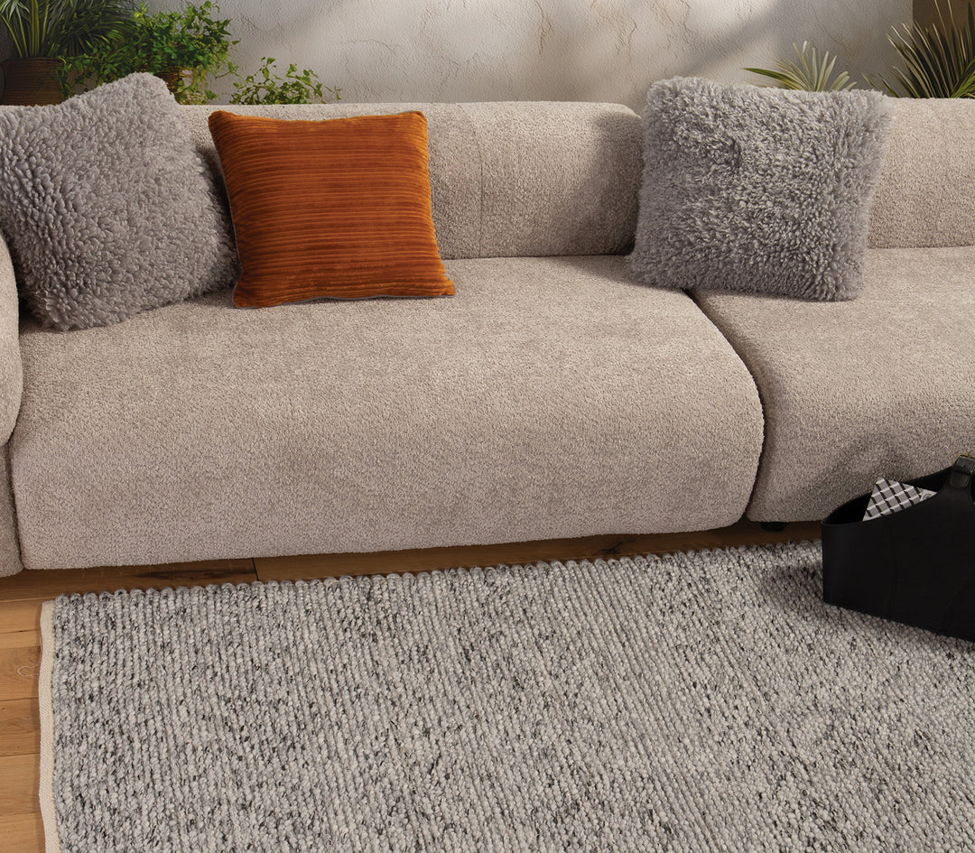 Σαλόνι με μπεζ καναπέ και διακοσμητικά μαξιλάρια, στο πάτωμα γκρι χαλί με φυσική πλεκτή υφή.