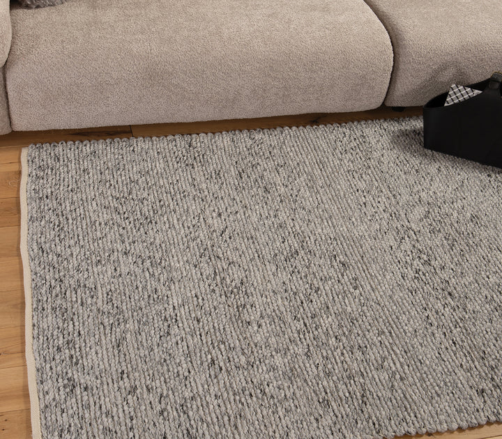 Διακόσμηση σαλονιού με γκρι χαλί με ανάγλυφα σχέδια, συνδυασμένα με ψάθινα καλάθια.