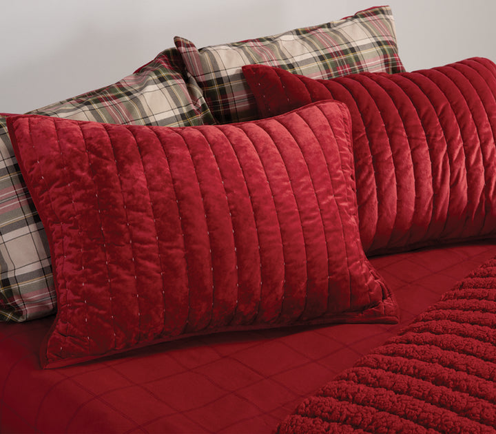 Κοντινό πλάνο από κόκκινες βελούδινες μαξιλαροθήκες με κάθετη ραφή, συνδυασμένες με καρό σεντόνια σε γήινους τόνους.