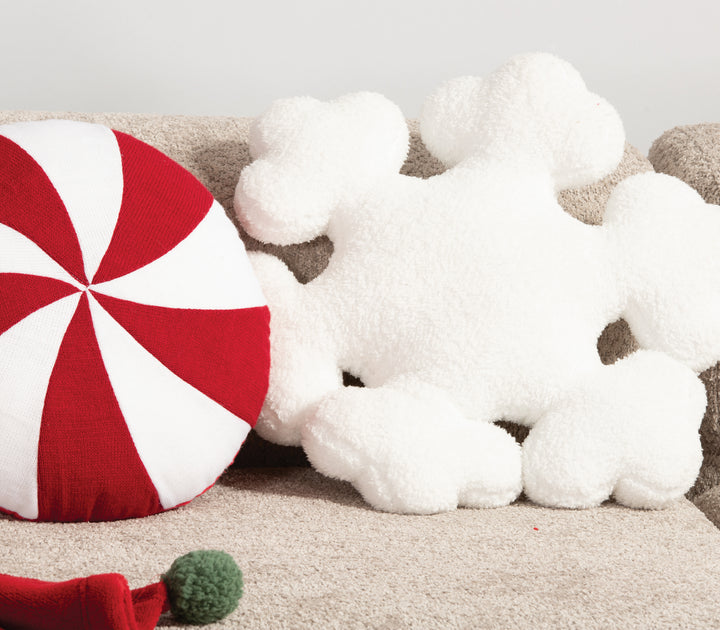 Λευκό αφράτο μαξιλάρι σε σχήμα χιονονιφάδας τοποθετημένο σε καναπέ, πλάι σε στρογγυλό μαξιλάρι κόκκινο-λευκό τύπου ζαχαρωτού