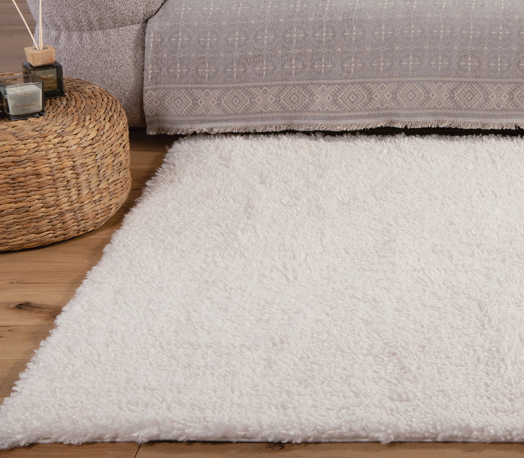 Λευκό χαλί σε καθιστικό με ξύλινο πάτωμα και στρογγυλό ψάθινο τραπεζάκι δίπλα σε γκρι καναπέ.