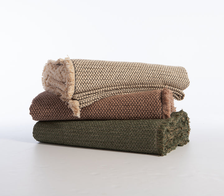 Τρία διπλωμένα ριχτάρια σε εκρού, καφέ και χακί χρώμα, τοποθετημένα το ένα πάνω στο άλλο.
