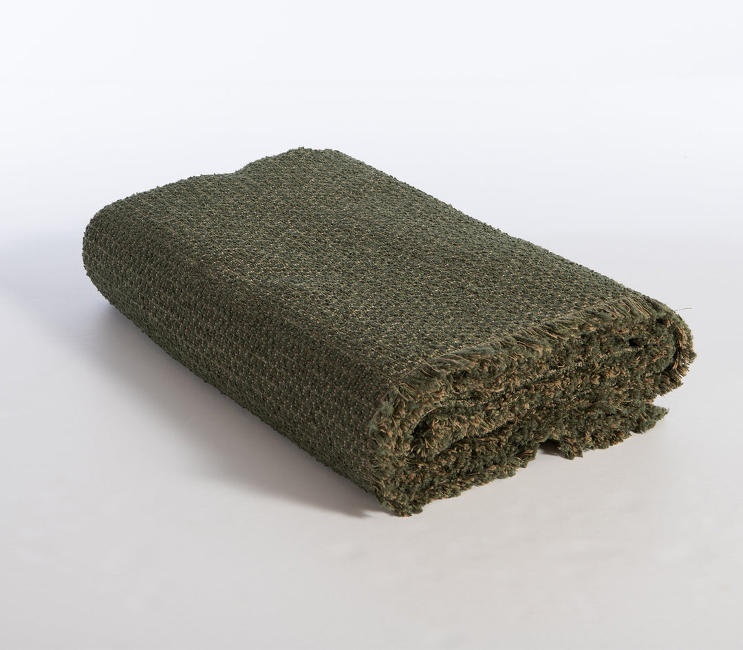 Διπλωμένο πράσινο ριχτάρι με πλέξη και κρόσσια στο τελείωμα.