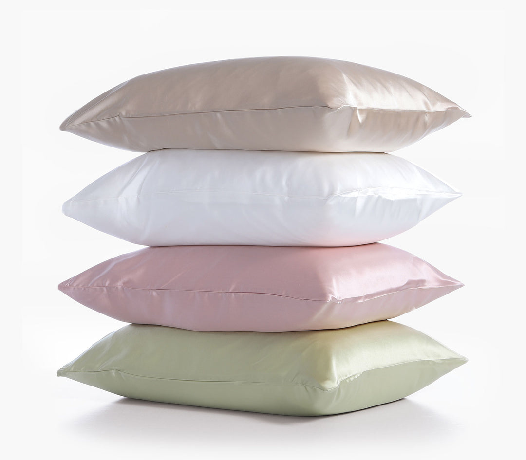 Στοίβα από μεταξωτές μαξιλαροθήκες σε παστέλ αποχρώσεις ροζ, λευκό, μπεζ και πράσινο σε καθαρό φόντο.