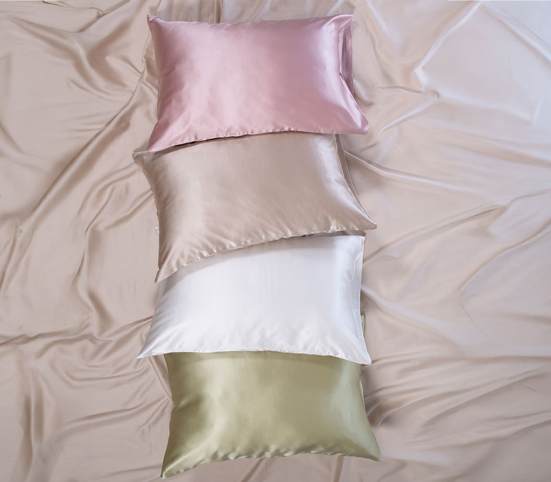 Μεταξωτές μαξιλαροθήκες σε διαφορετικές αποχρώσεις τοποθετημένες πάνω σε σατέν σεντόνι με απαλή υφή.