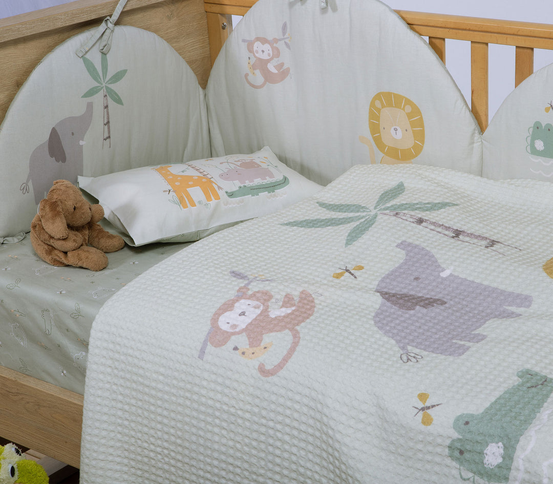 Βρεφική πικέ κουβέρτα με ζωάκια ζούγκλας τοποθετημένη μέσα σε ξύλινη κούνια δίπλα σε λούτρινο παιχνίδι.