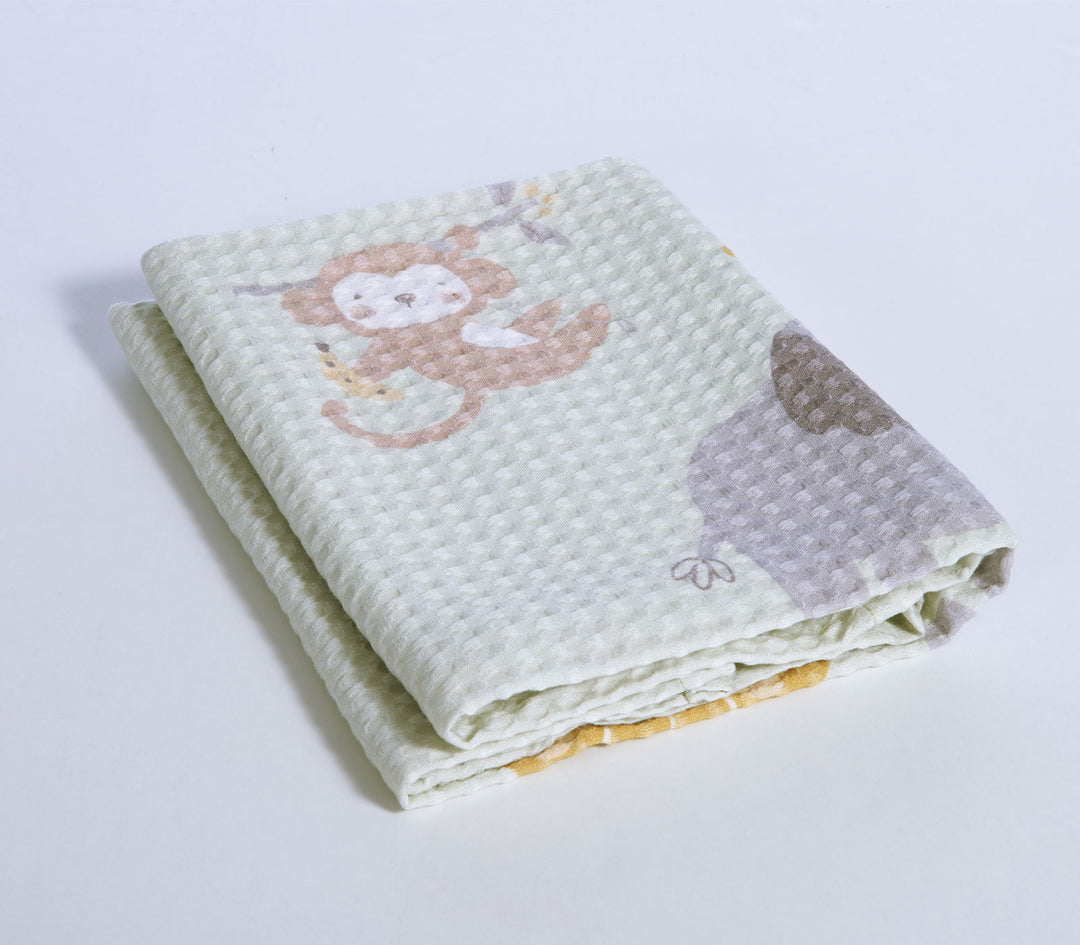 Διπλωμένη βρεφική πικέ κουβέρτα με χαριτωμένο σχέδιο μαϊμού και ζωάκια ζούγκλας σε λευκό φόντο.