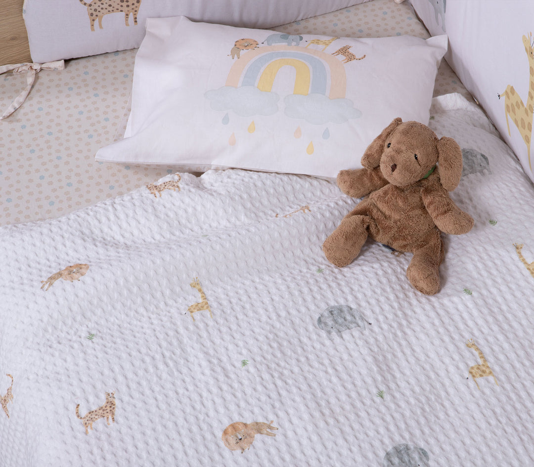 Βρεφική πικέ κουβέρτα αγκαλιάς με ζωάκια ζούγκλας τοποθετημένη σε κούνια δίπλα σε μαξιλάρι και λούτρινο παιχνίδι.