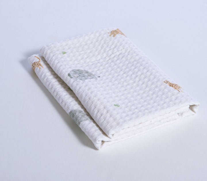 Διπλωμένη βρεφική πικέ κουβέρτα κούνιας με ανάγλυφη υφή και σχέδιο ζωάκια ζούγκλας σε λευκό φόντο.