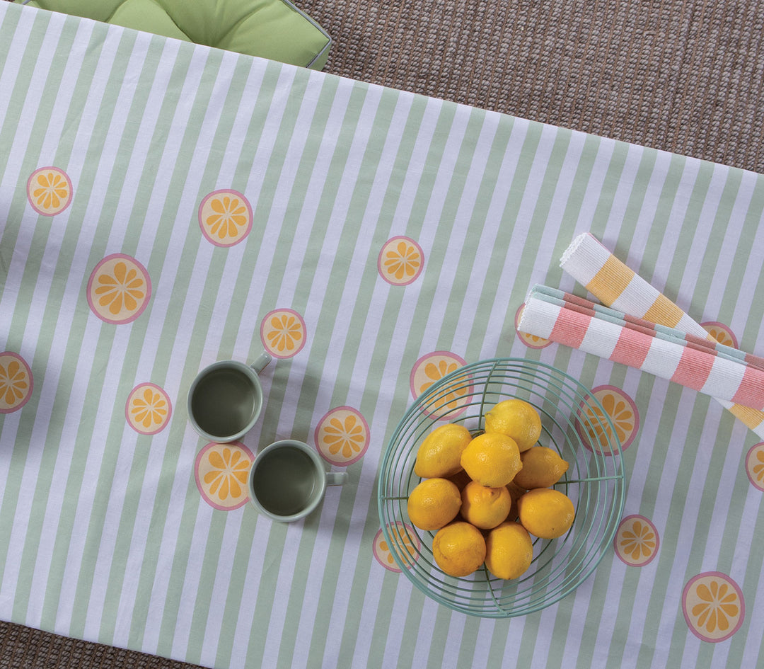 Κοντινή λήψη τραπεζομάντηλου ριγέ μέντα με λεμόνια, με μπολ φρούτων και φλιτζάνια πάνω σε υφασμάτινη επιφάνεια.