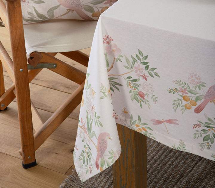 Κοντινό σε εκρού τραπεζομάντηλο με floral μοτίβο και πουλιά πάνω σε ξύλινο τραπέζι με καρέκλα δίπλα.