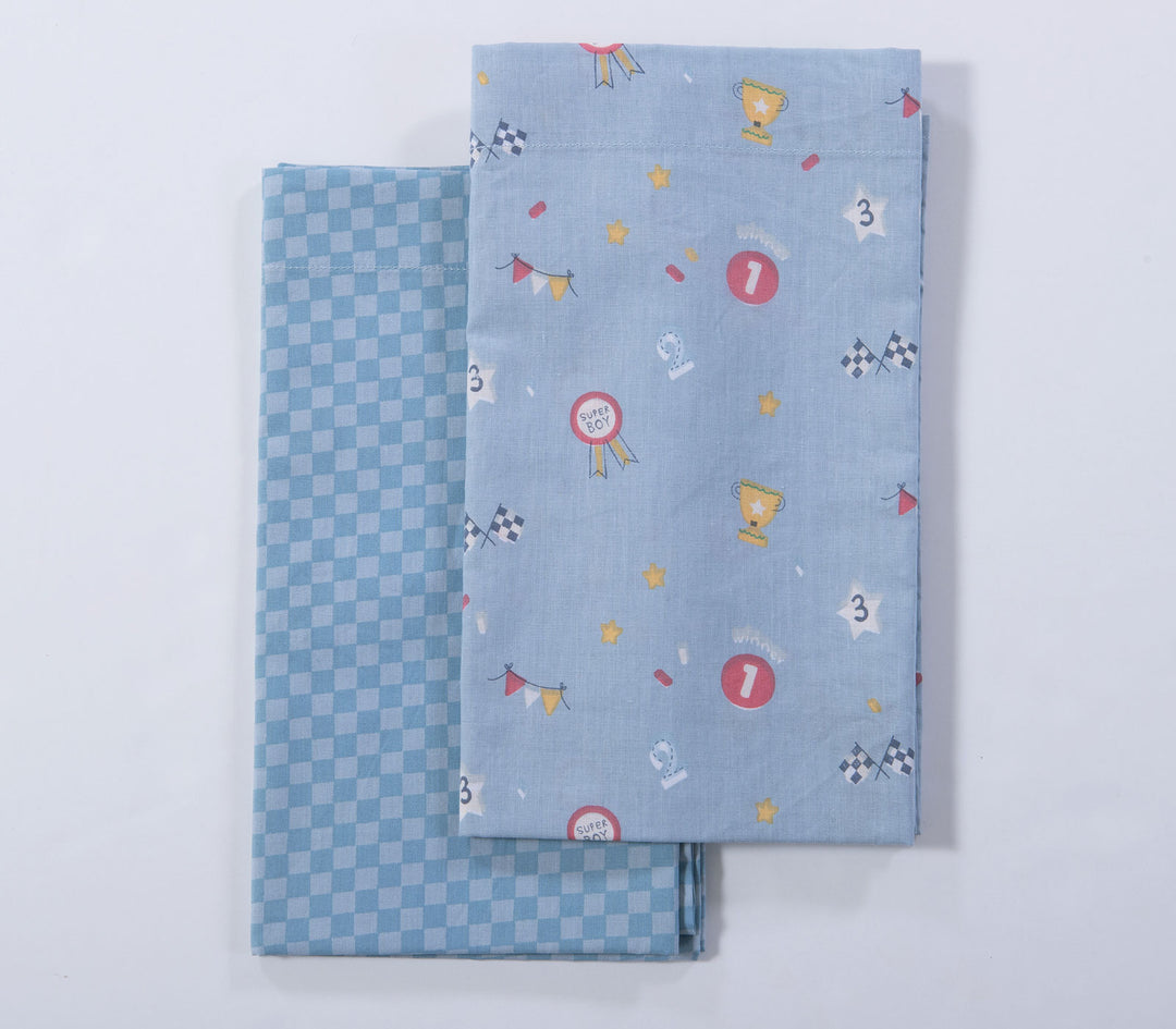 Διπλωμένα γαλάζια βρεφικά σεντόνια λίκνου με μοτίβα τρόπαια, σημαιάκια αγώνα και καρό σχέδιο σε λευκό φόντο.