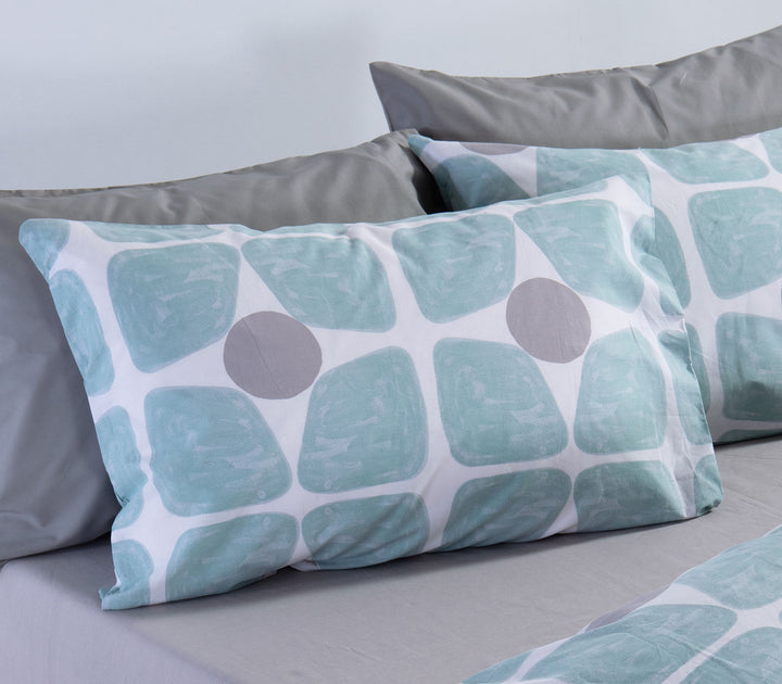 Μαξιλαροθήκη ύπνου τιρκουάζ και γκρι με γεωμετρικό μοτίβο πάνω σε κρεβάτι με γκρι σεντόνια.