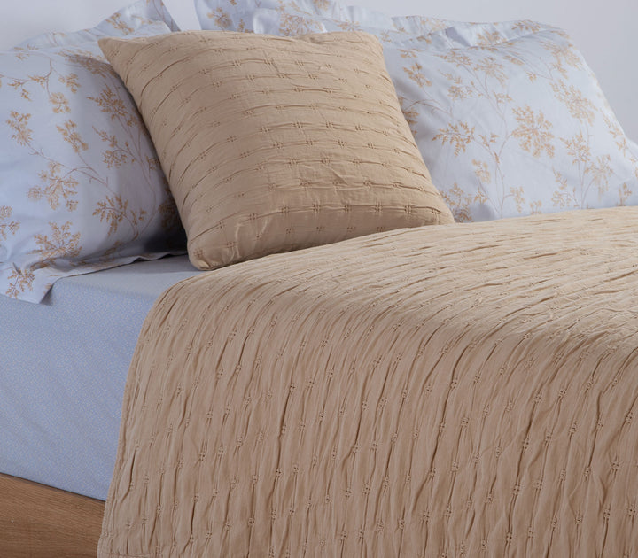 Κίτρινο διακοσμητικό μαξιλάρι Foxy με ανάγλυφη υφή πάνω σε κρεβάτι με γαλάζια παπλωματοθήκη floral σχεδίου.