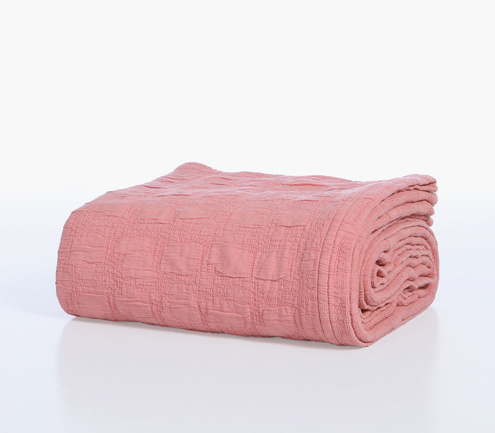 Διπλωμένη βαμβακερή κουβέρτα Nef-Nef Homeware σε κοραλί απόχρωση με ανάγλυφη ζακάρ υφή πάνω σε λευκό φόντο.