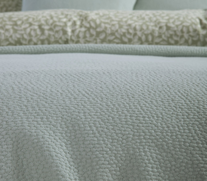 Κοντινή λήψη υφής βαμβακερής κουβέρτας Nef-Nef Homeware σε πράσινη απόχρωση με διακριτικό ανάγλυφο μοτίβο.