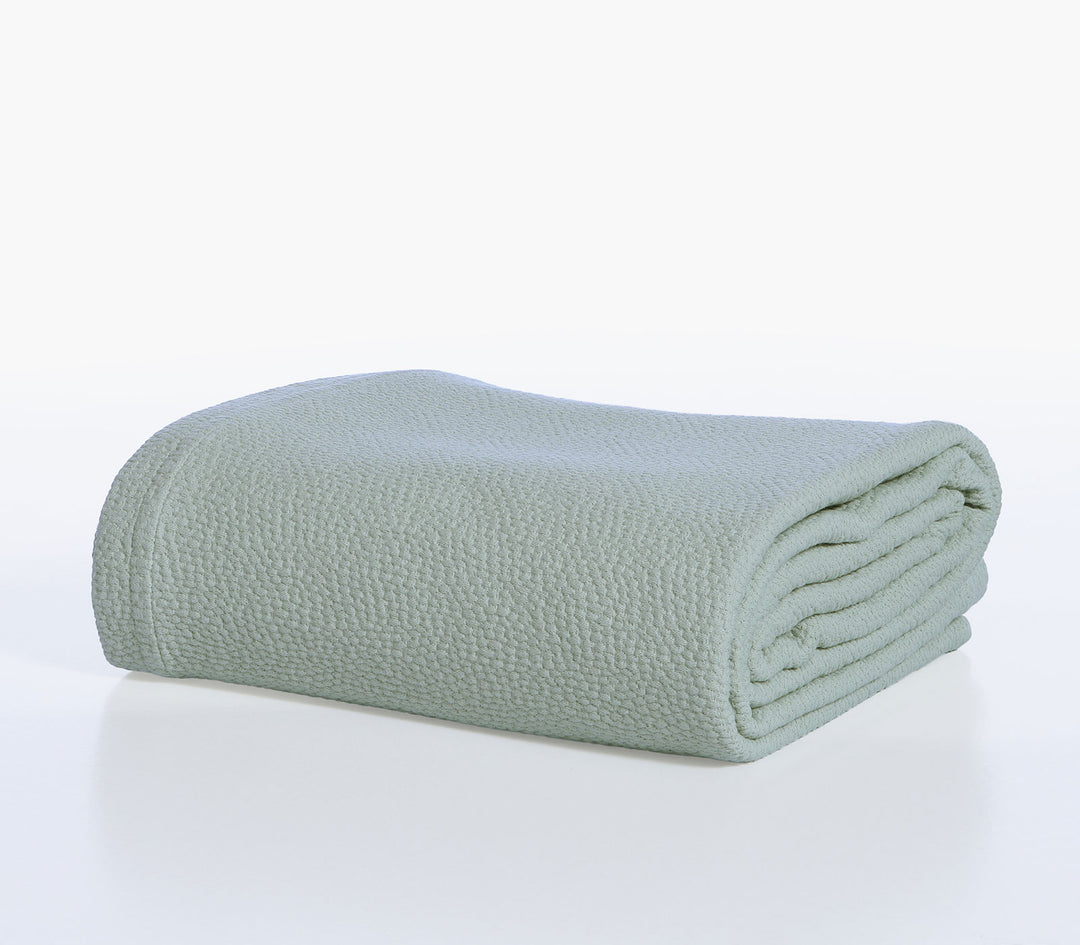 Διπλωμένη βαμβακερή κουβέρτα Nef-Nef Homeware σε πράσινη απόχρωση τοποθετημένη σε λευκό φόντο.